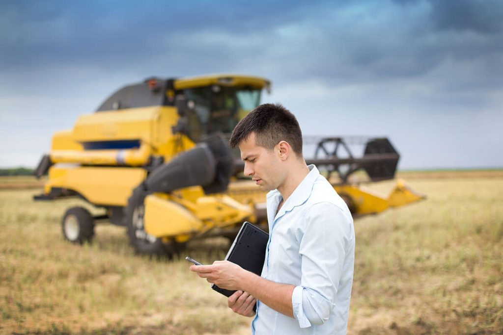 famer checking his phone outside, harvester in the background