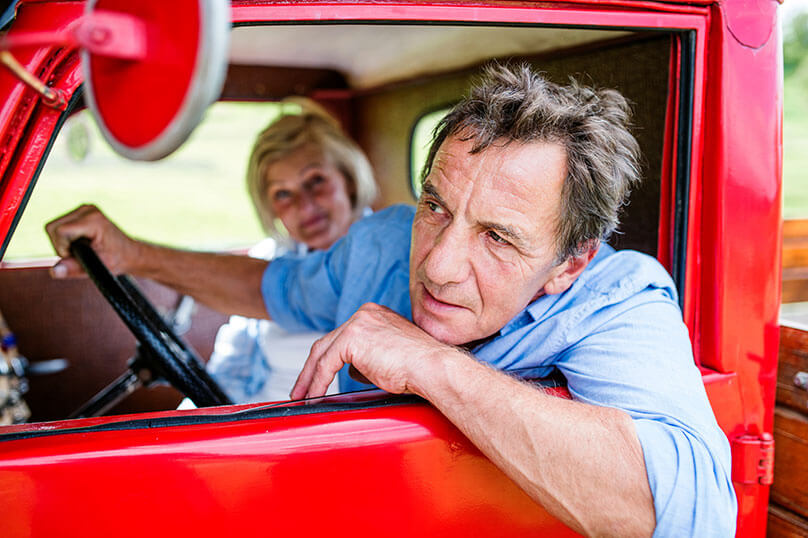 farmer looking out of car window, red car